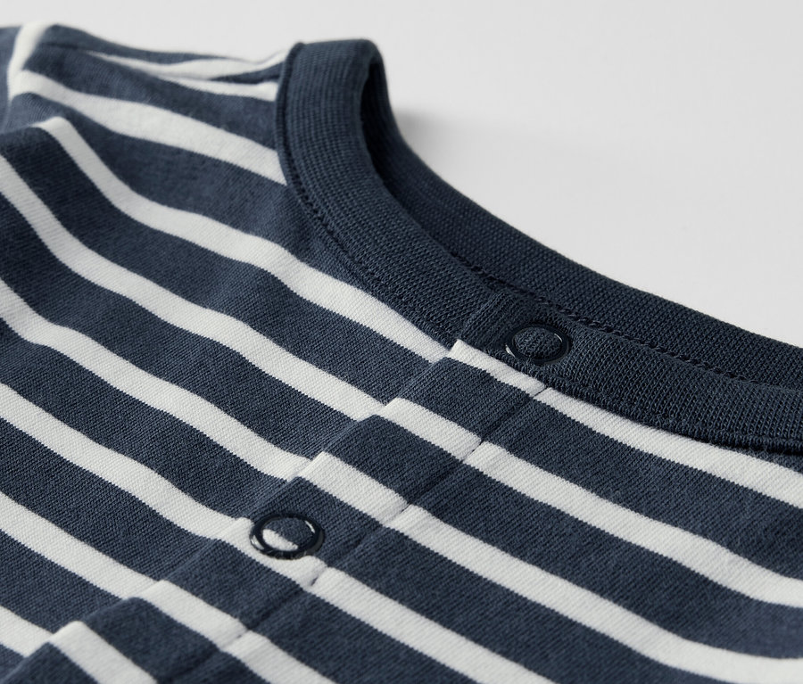 Detail kojenecké soupravy s modrými a bílými pruhy a zapínáním na druky.