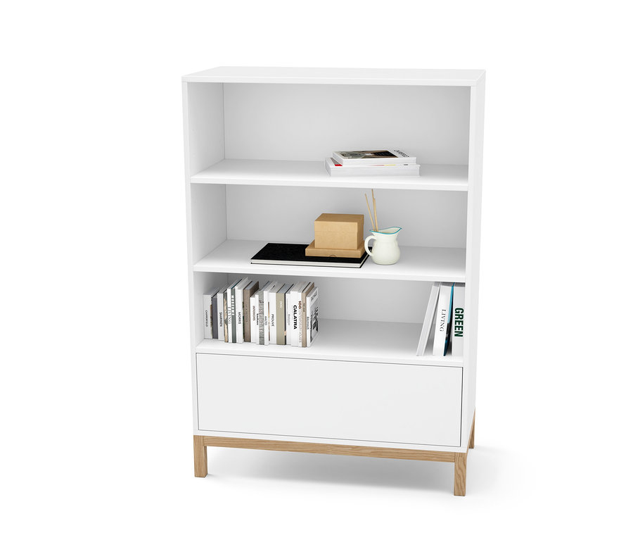 Bílá komoda se zásuvkou a policemi, na kterých jsou knihy a dekorace.