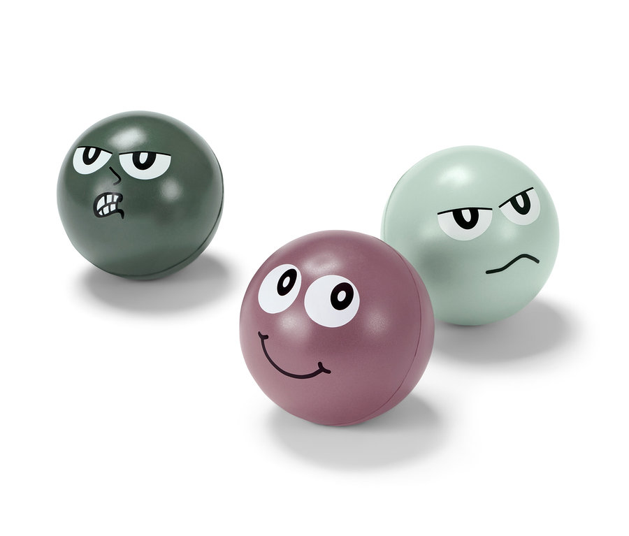 Tři antistresové míčky s obličeji. Jeden je zelený s naštvaným výrazem, druhý fialový s usměvavým výrazem a třetí světle zelený s otráveným výrazem.