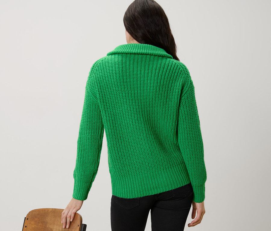 Žena stojí zády a má na sobě zelený svetr troyer z hrubého úpletu.
