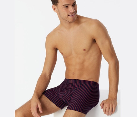 Muž sedí a má na sobě červené trenýrky SCHIESSER s biobavlnou.