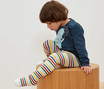 Chlapec sedí na dřevěné stoličce a má na sobě pruhované punčocháče.