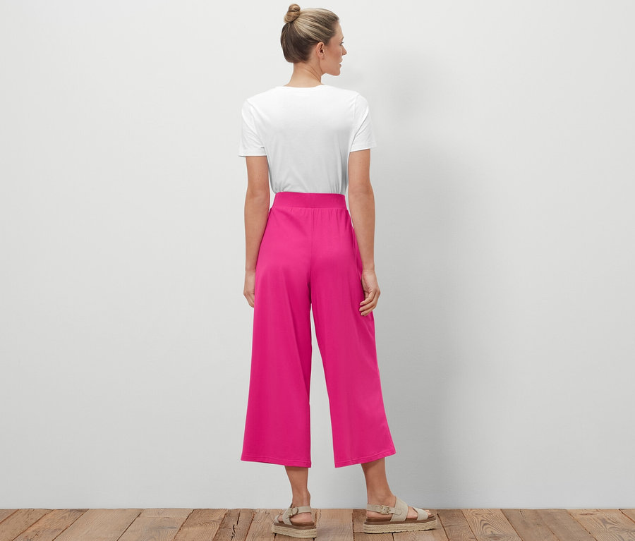 Žena stojí zády k fotoaparátu a má na sobě žerzejové kalhoty culotte.