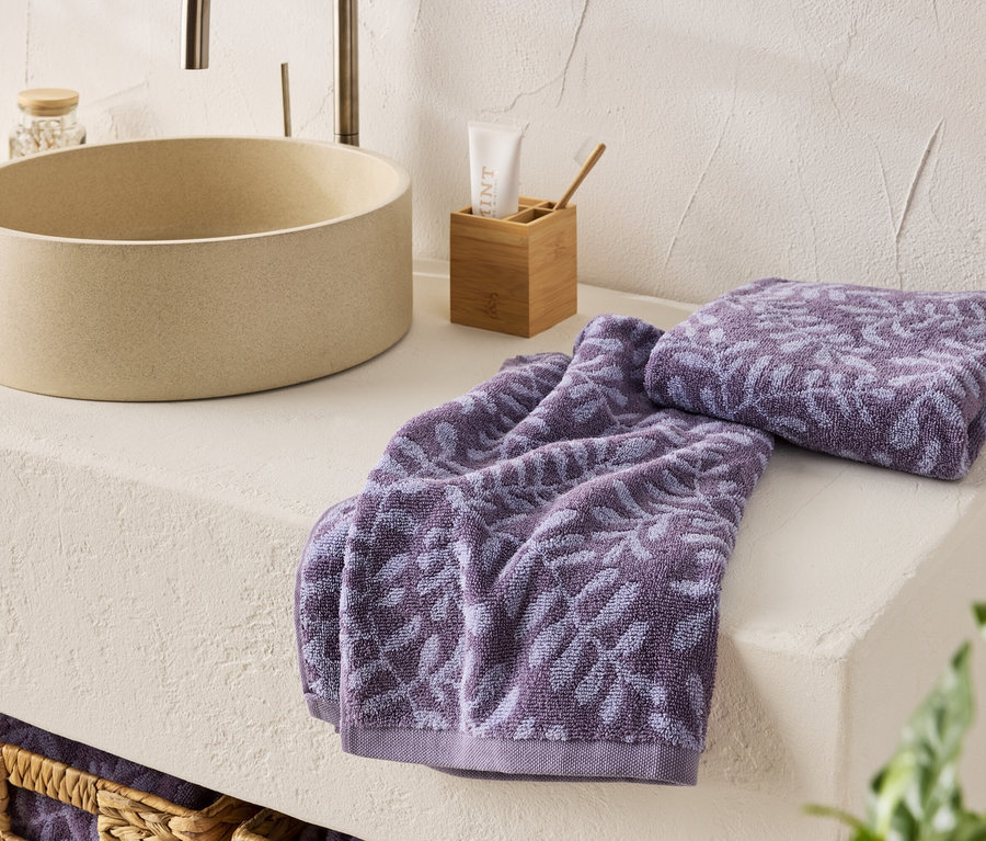 Dva fialové ručníky s květinovým vzorem leží vedle umyvadla.