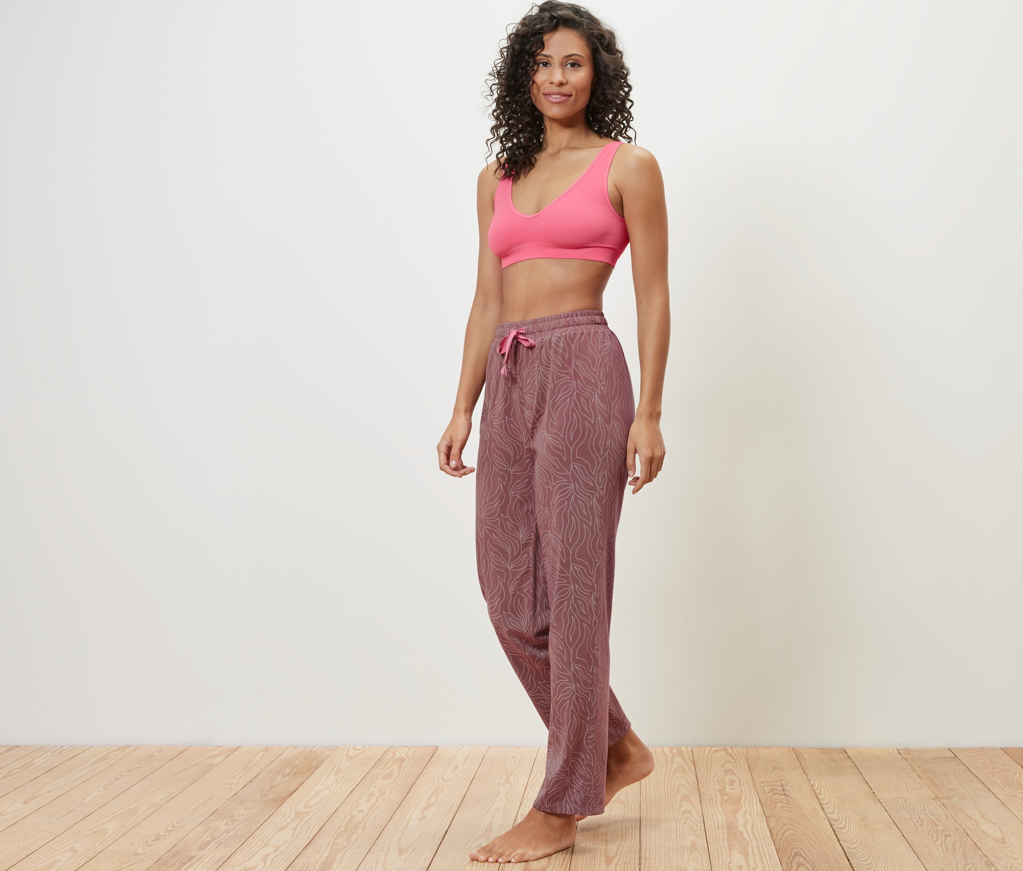 Žena pózuje v růžové sportovní podprsence a pyžamových kalhotách.