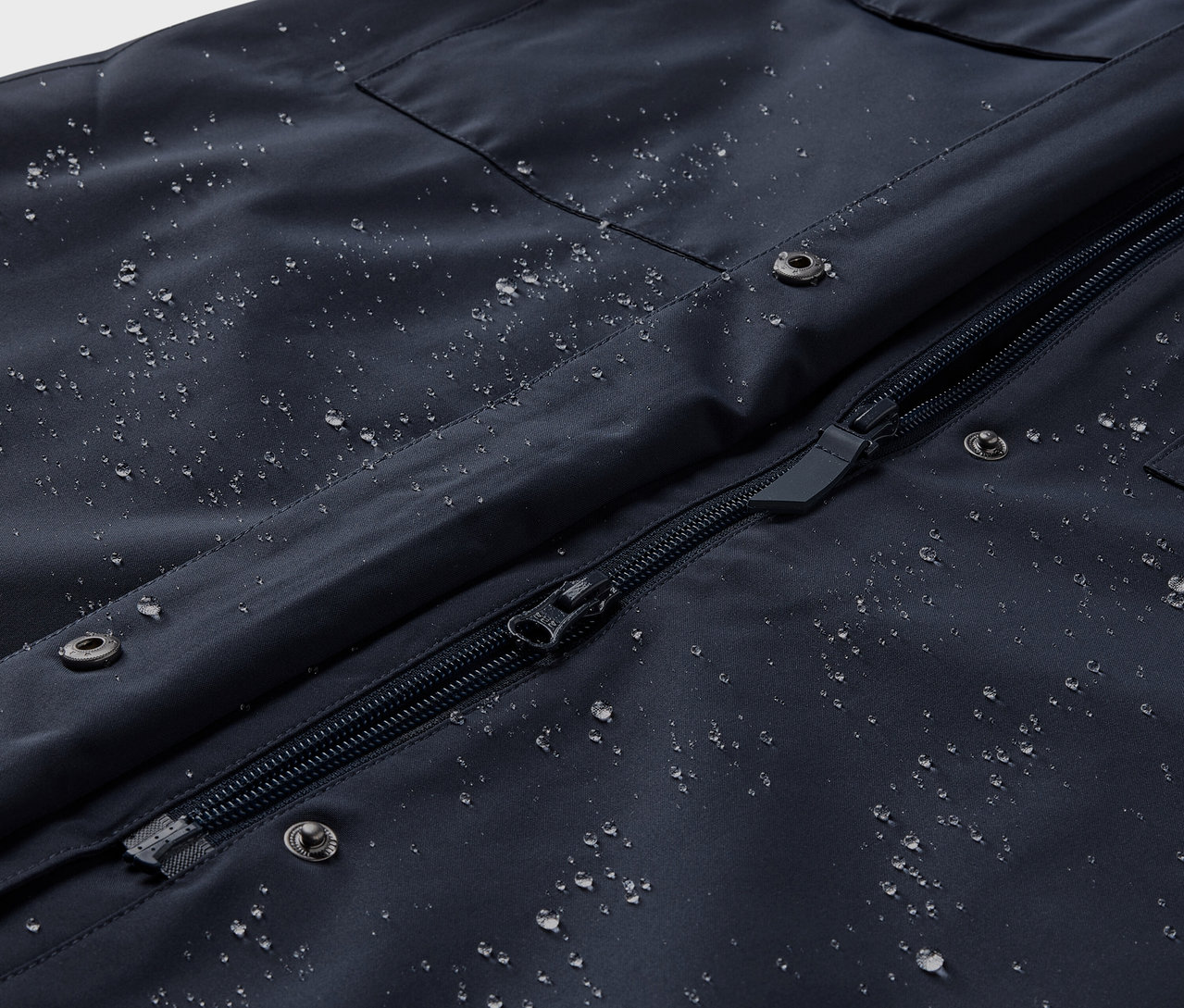 Detailní pohled na nepromokavý trenčkot s kapkami vody.