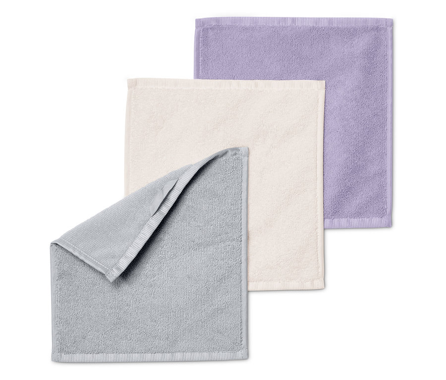 Tři ručníky složené na sobě: šedý, krémový a fialový.