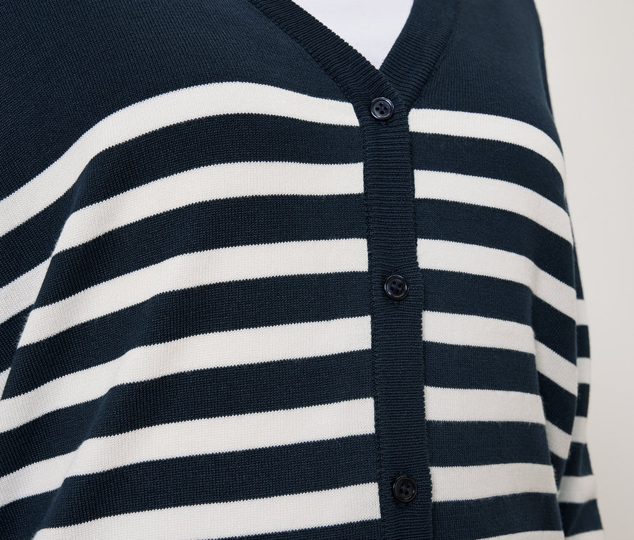 Detail modrého svetru s bílými pruhy a knoflíky.