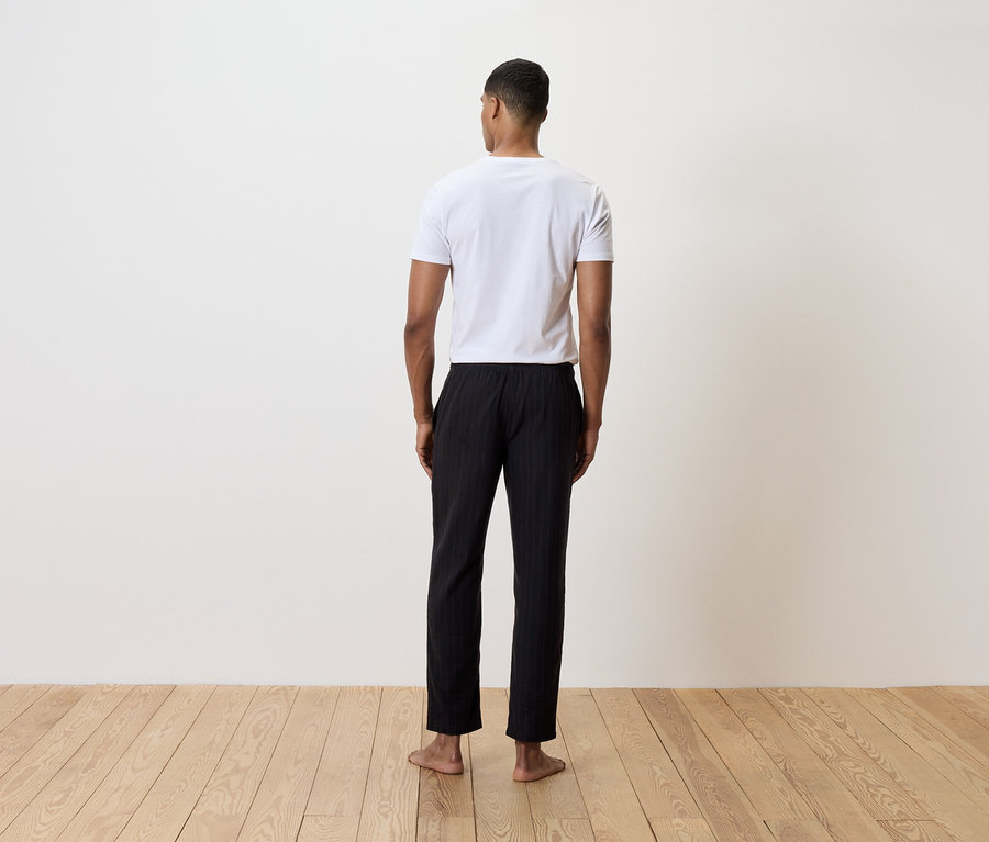 Muž stojí zády k fotoaparátu a má na sobě bílé tričko a černé pruhované kalhoty.