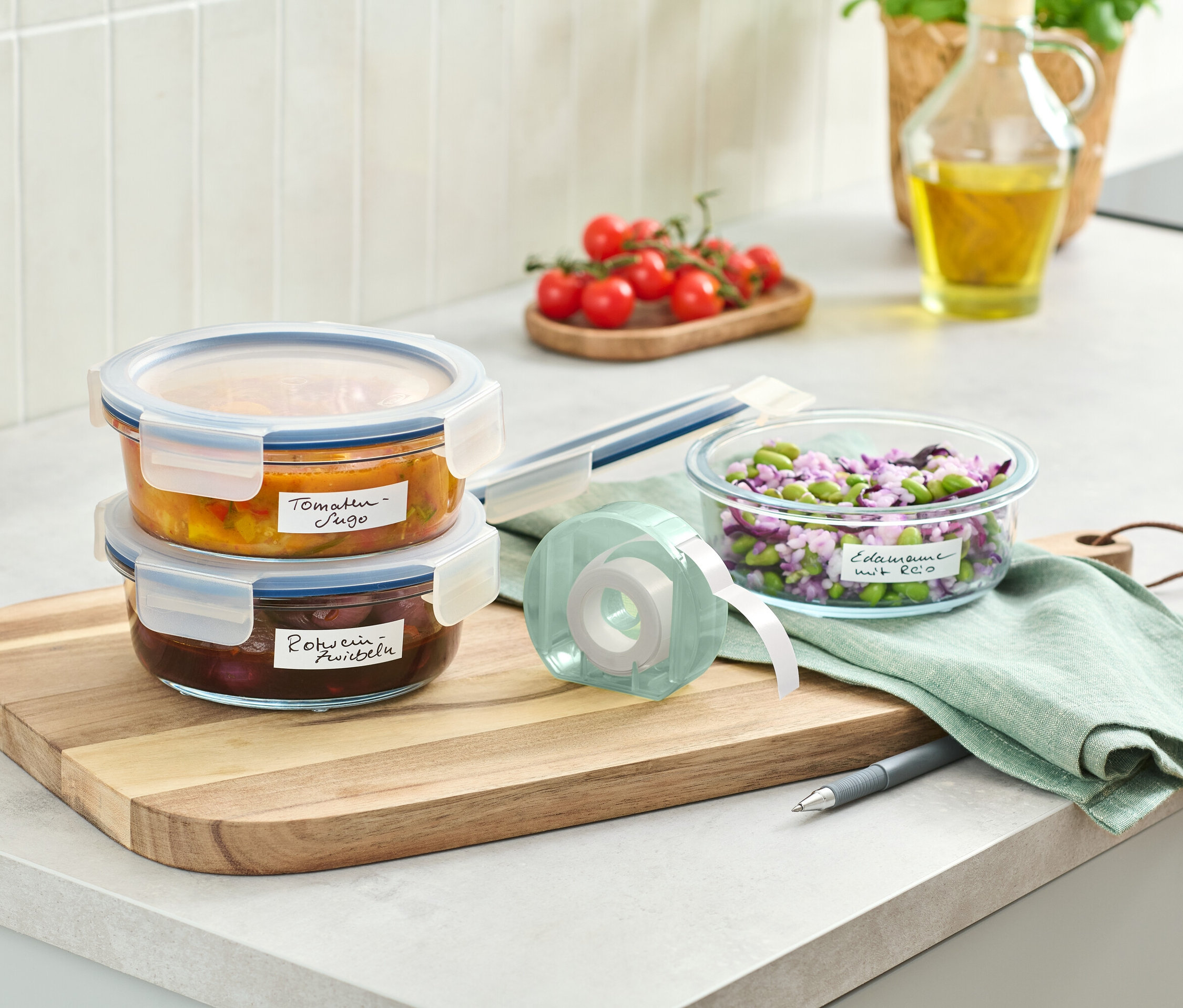 Dva skleněné zásobníky s jídlem naskládané na dřevěném prkénku vedle role s etiketami.