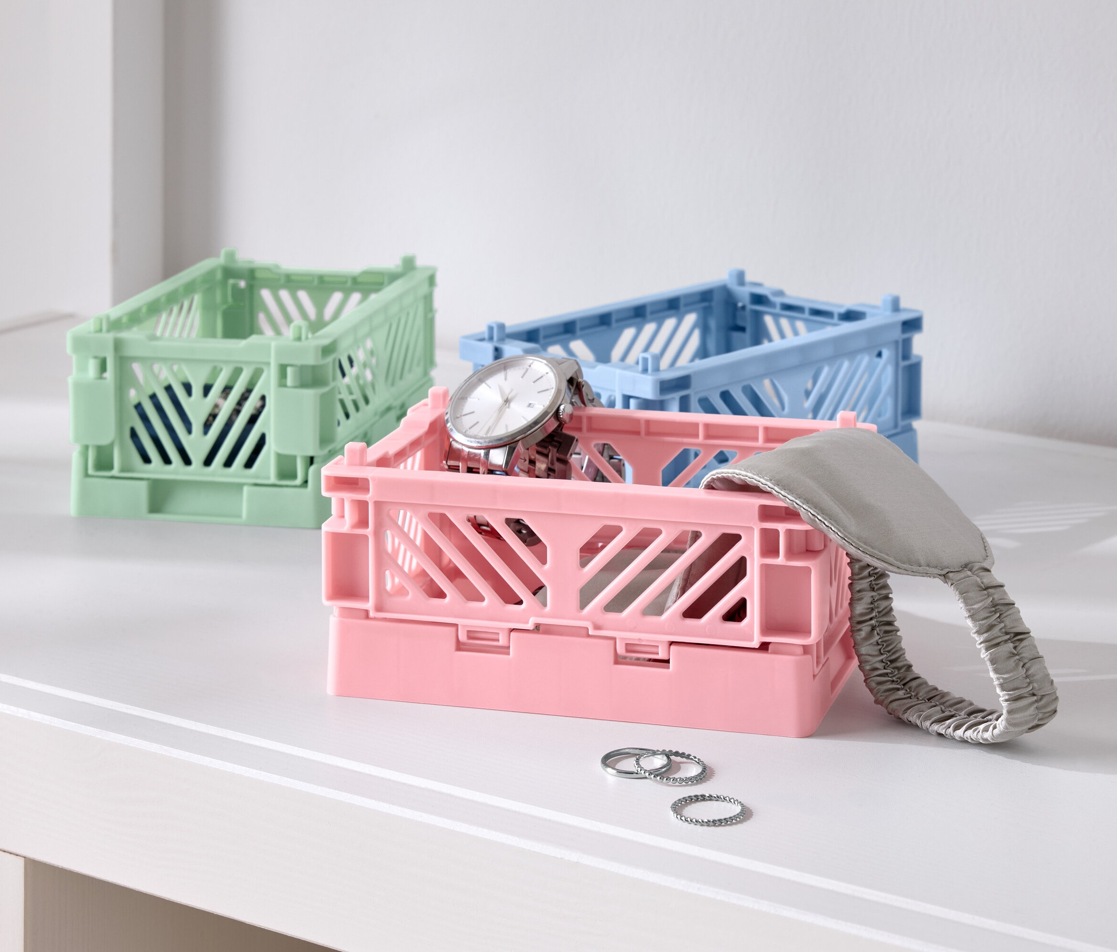 Tři barevné skládací krabice na stole, jedna růžová s hodinkami, jedna modrá a jedna zelená.