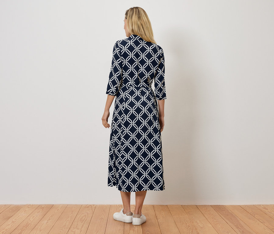 Zezadu je vidět žena v námořnicky modrých šatech s bílým geometrickým vzorem a bílých teniskách.