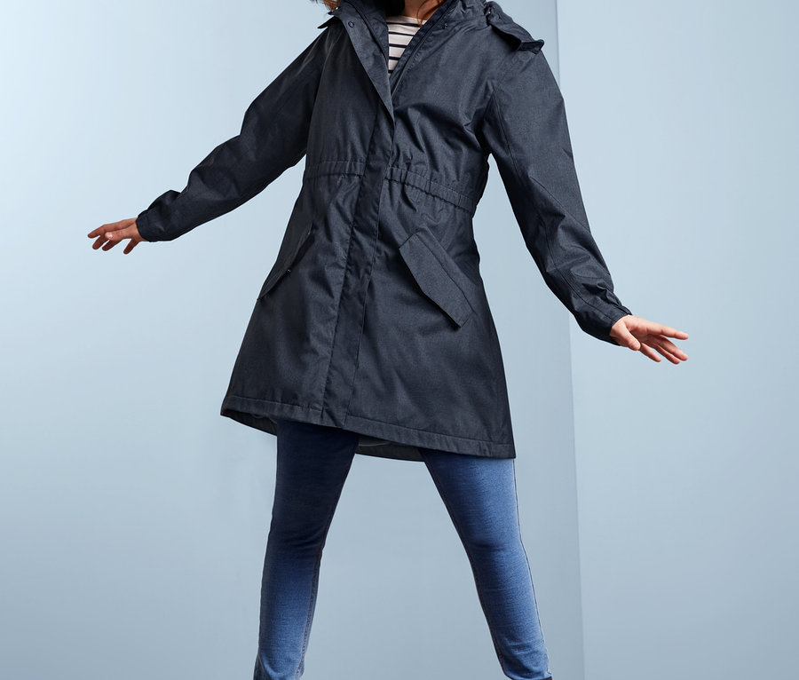 Usmívající se dívka pózuje v džínové bundě do každého počasí, modrých džínách a botách.