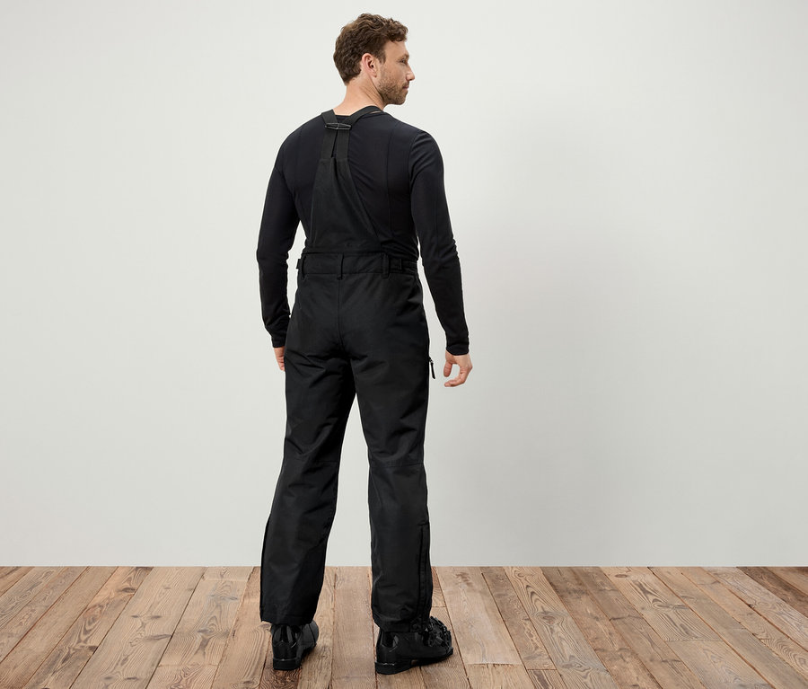 Muž zády k fotoaparátu má na sobě černé lyžařské kalhoty s laclem a černé lyžařské boty.