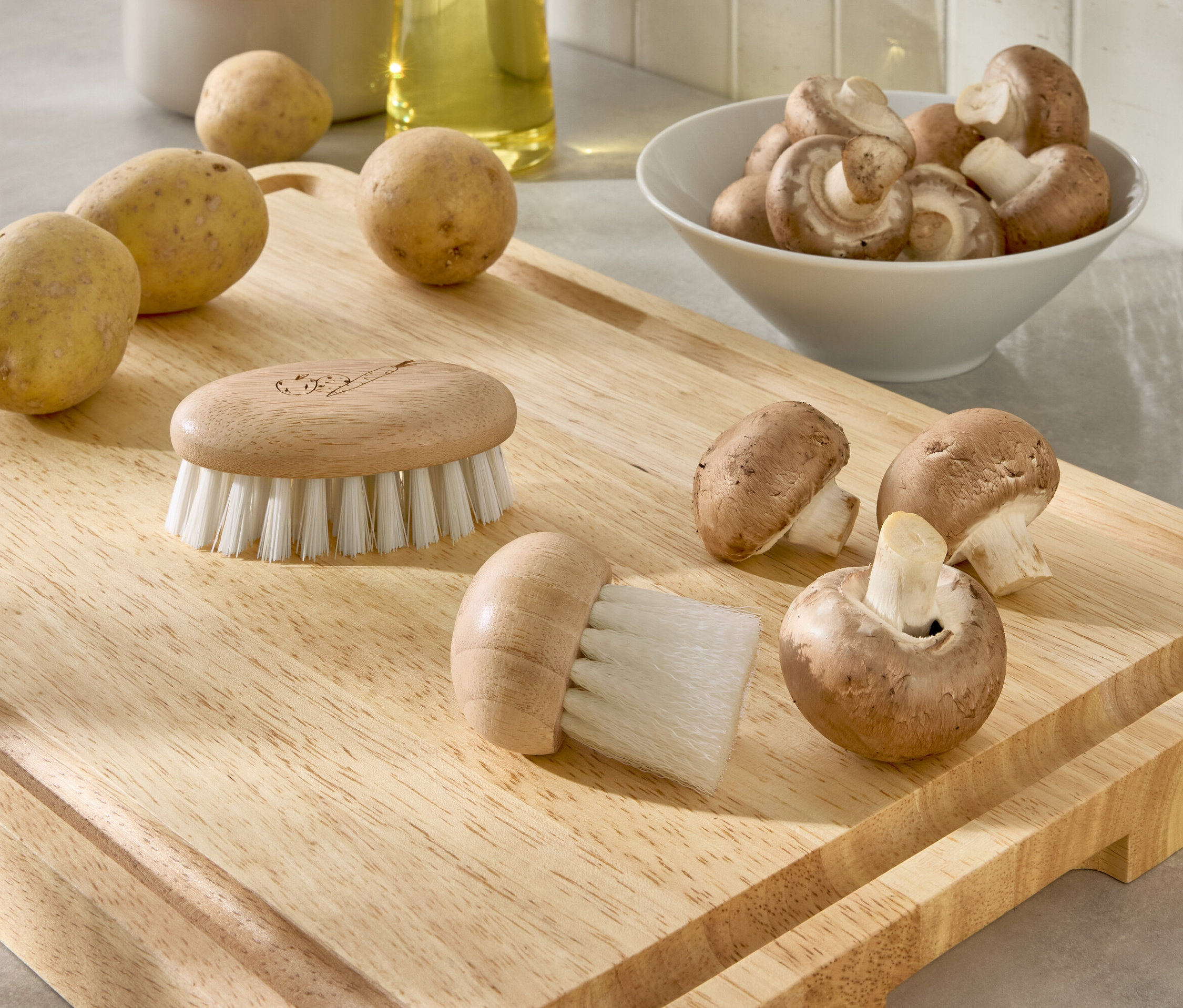 Na dřevěném prkénku leží brambory, houby a dva kartáče.