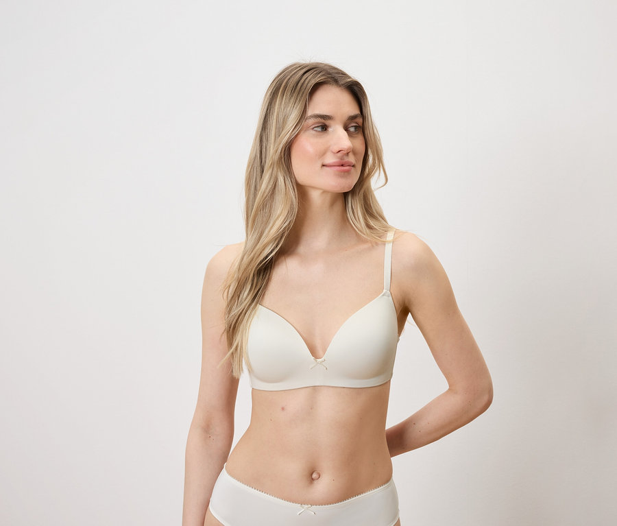 Žena s blond vlasy a světlou pletí pózuje ve světlé podprsence a kalhotkách.
