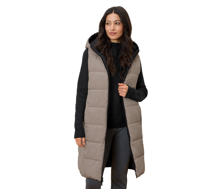 Žena stojící a má na sobě dlouhou prošívanou vestu s kapucí.