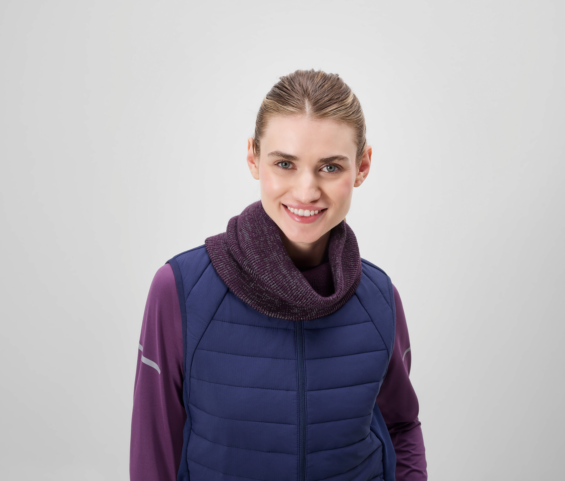 Usmívající se žena má na sobě fialový rolák a modrou prošívanou vestu.