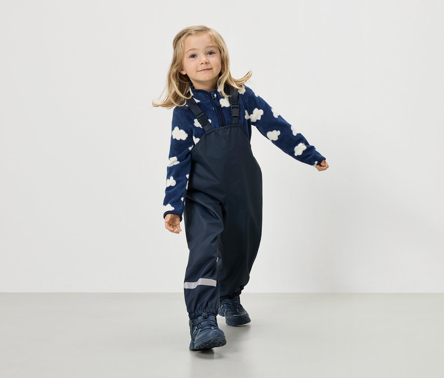 Blonďatá dívka má na sobě tmavě modrou fleecovou bundu s oblačným vzorem a tmavě modré kalhoty s laclem.