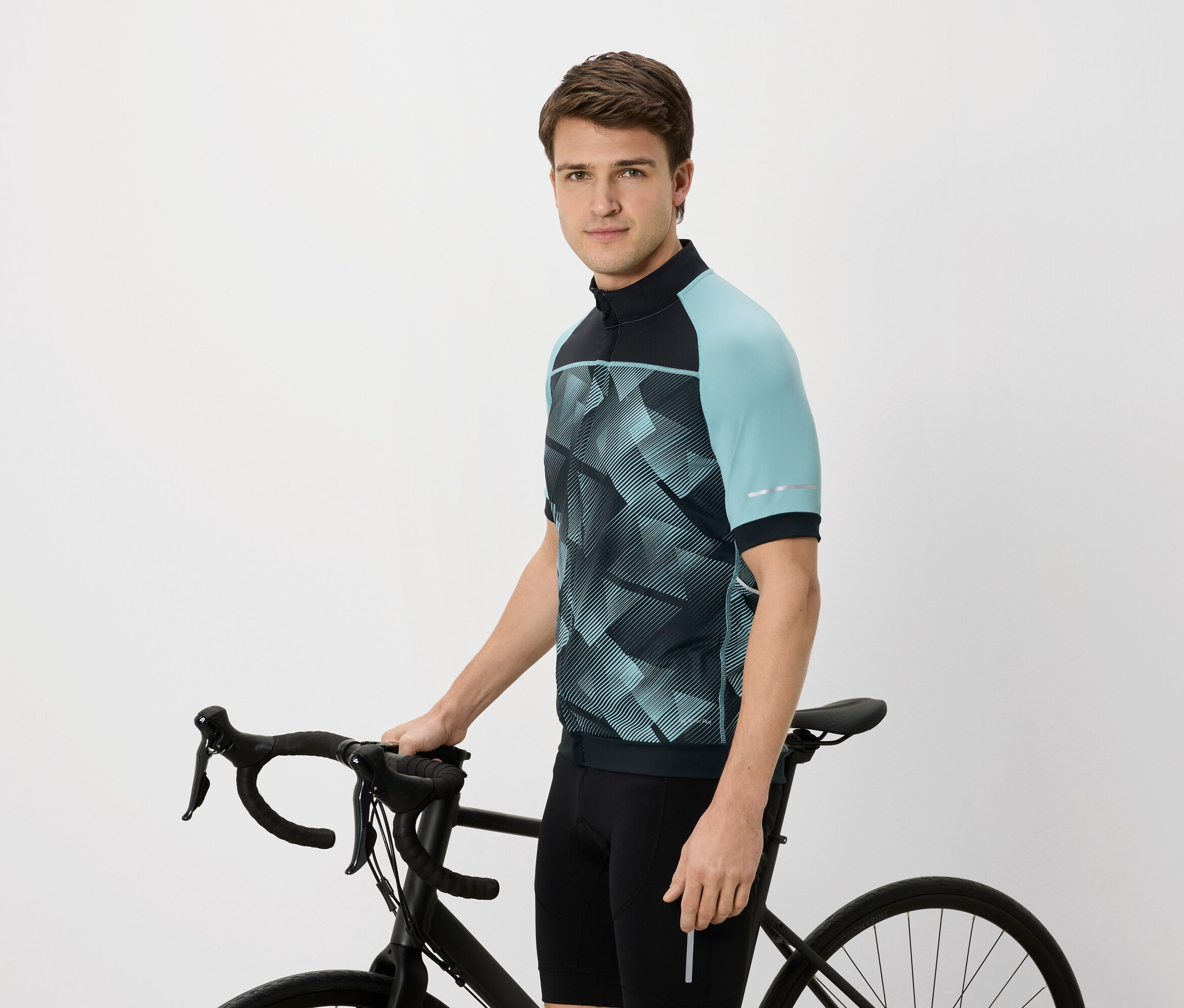 Muž v cyklistickém dresu s modrozelenými rukávy drží černé kolo.