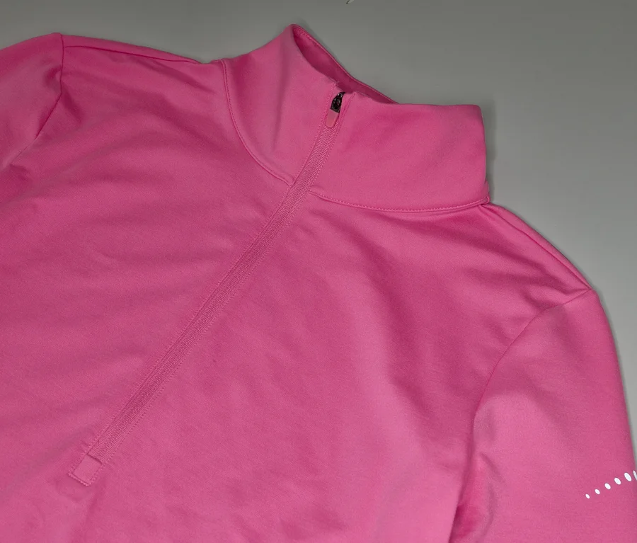 Růžový sportovní top s dlouhým rukávem, krátkým zipem u krku a bílými tečkami na rukávu.