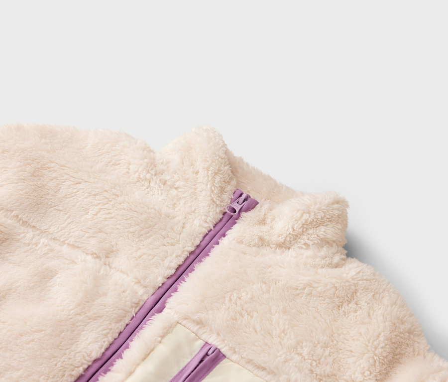 Detailní záběr krémové fleecové bundy s fialovým zipem.