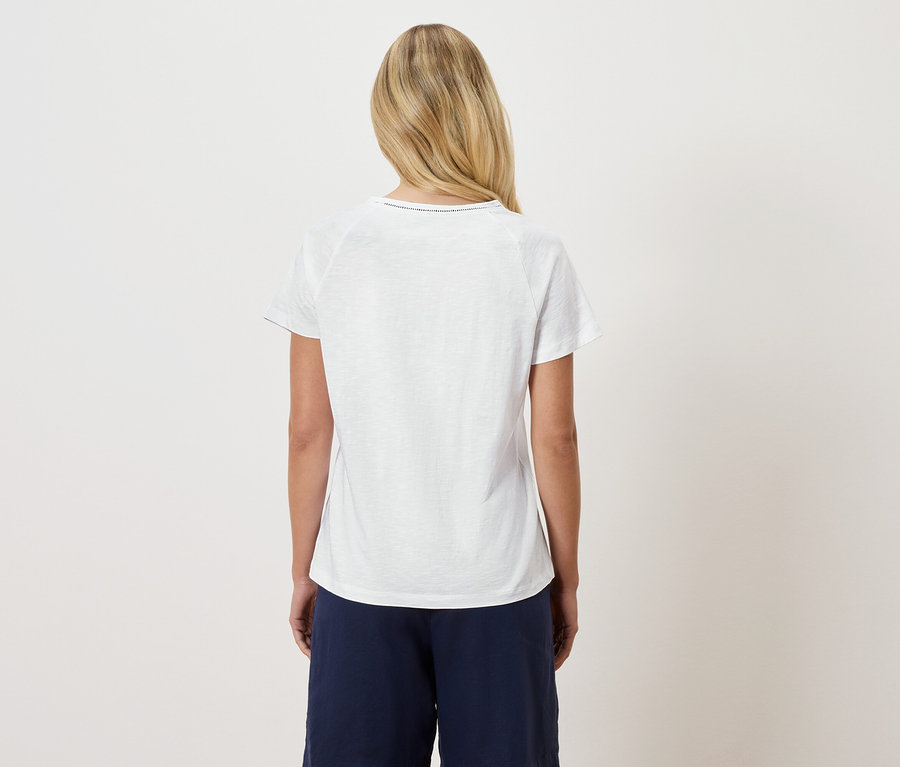 Pohled zezadu na blondýnu v bílém tričku a tmavě modrých kalhotách.