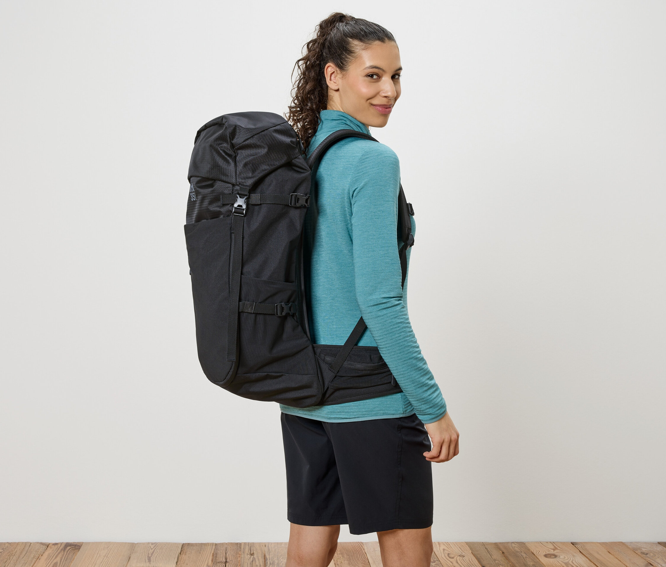 Žena s černým batohem přehozeným přes ramena se dívá přes rameno.