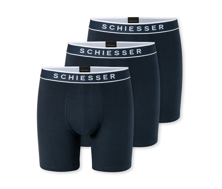 Tři tmavě modré boxerky s bílými pasy, každé s logem „SCHIESSER“, jsou naskládané a mírně se překrývají na bílém pozadí.