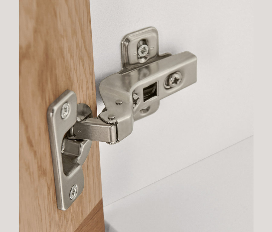 Detail stříbrného pantu na vysoké skříňce se 2 dvířky.