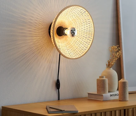 Nástěnná lampa s bambusovým stínítkem visí na zdi nad dřevěnou komodou.