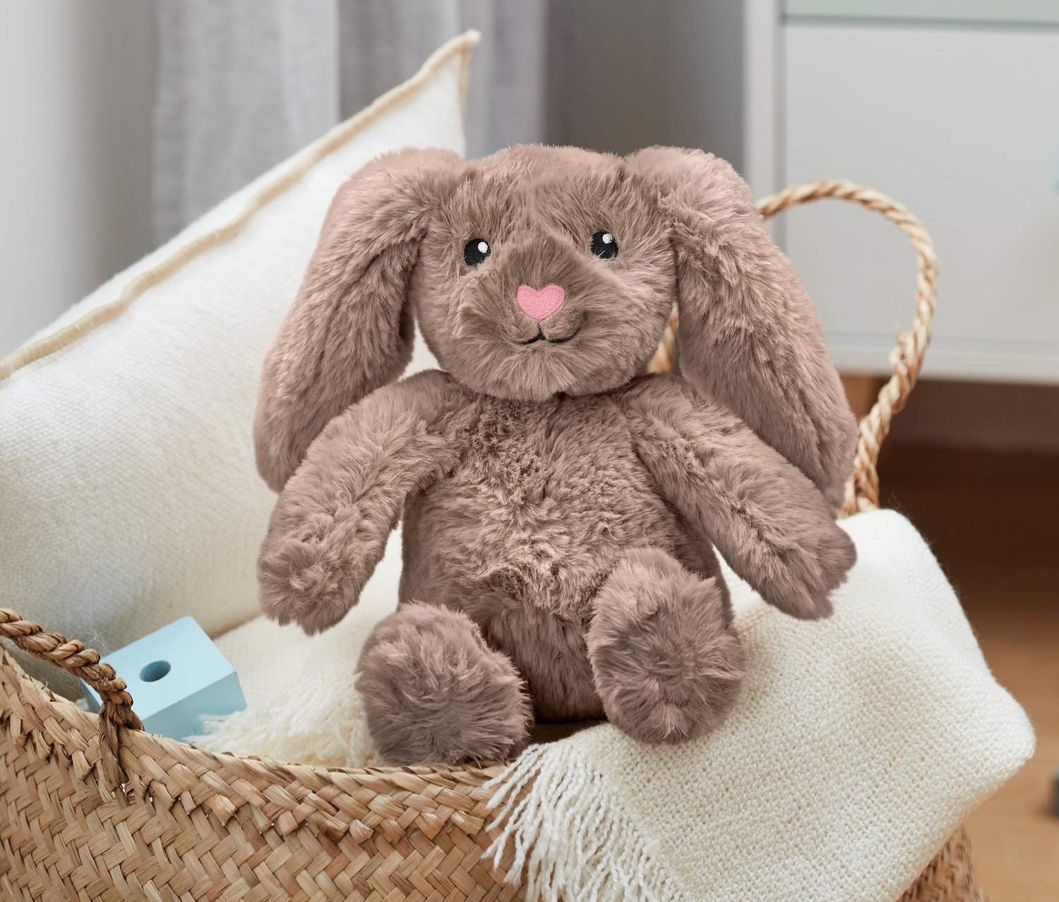 Plyšový zajíc sedí v proutěném košíku na bílé dece vedle dřevěných kostek.