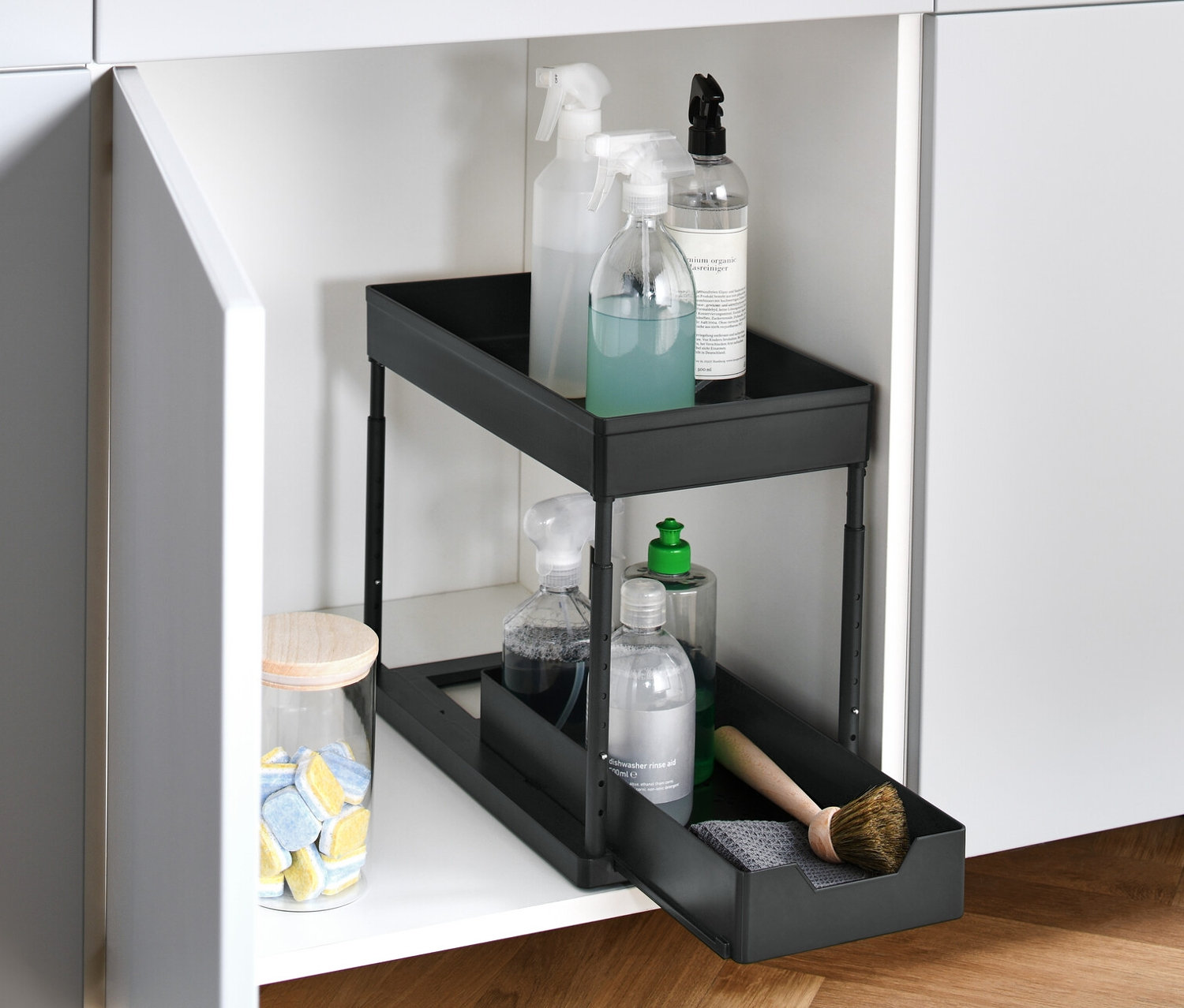 Otevřená bílá skříňka, v ní výsuvná zásuvka do skříňky se čisticími prostředky.