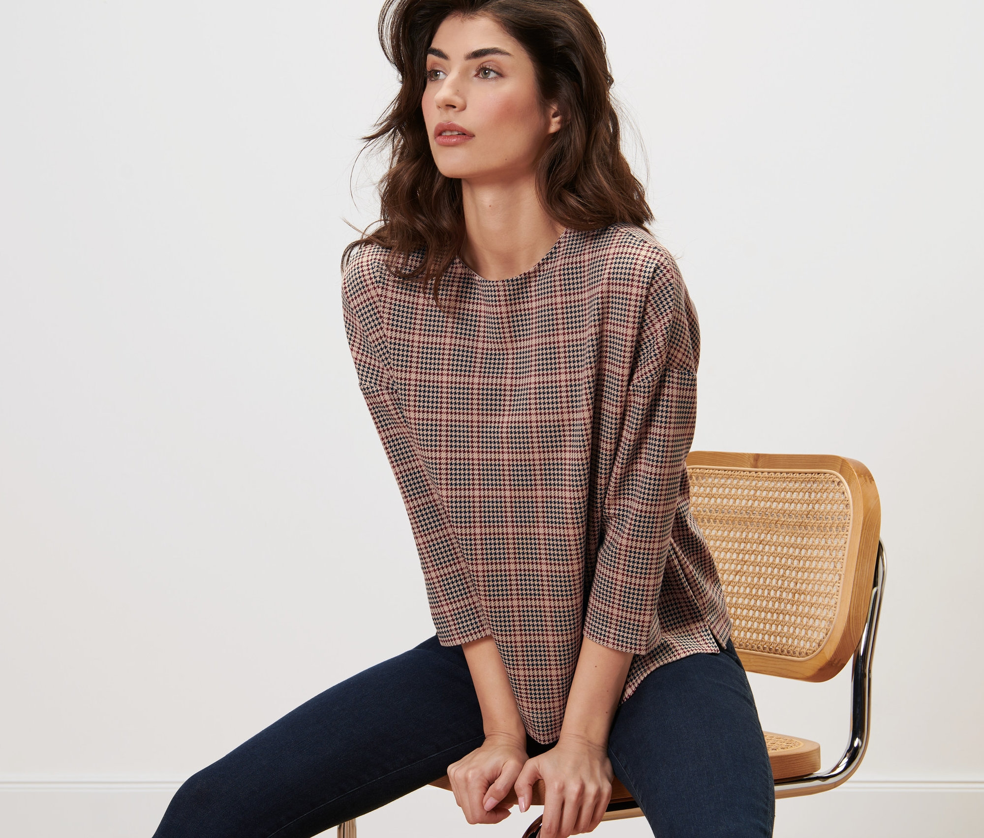 Žena sedí na židli a má na sobě mikinu s 3/4 rukávem a kohoutí stopou.