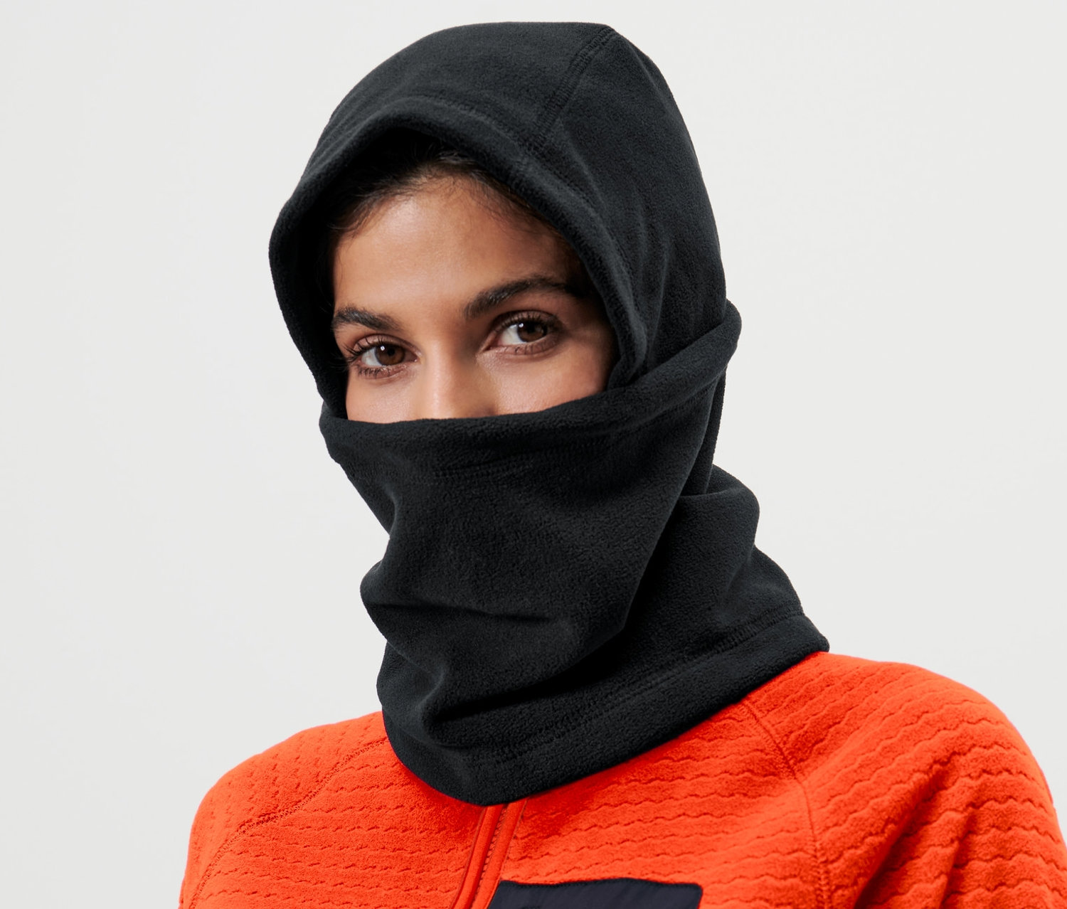 Žena má na sobě černou mikroflísovou kuklu a oranžovou bundu.