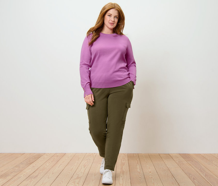 Žena pózuje v jemném svetru a khaki joggpantech s cargo kapsami.