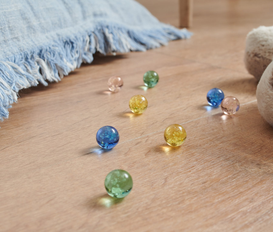 Na podlaze leží světelné kuličky různých barev vedle plyšového psa a modré deky.