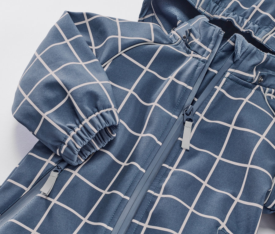 Detail dětské softshellové kombinézy s kostkovaným vzorem a zipem.