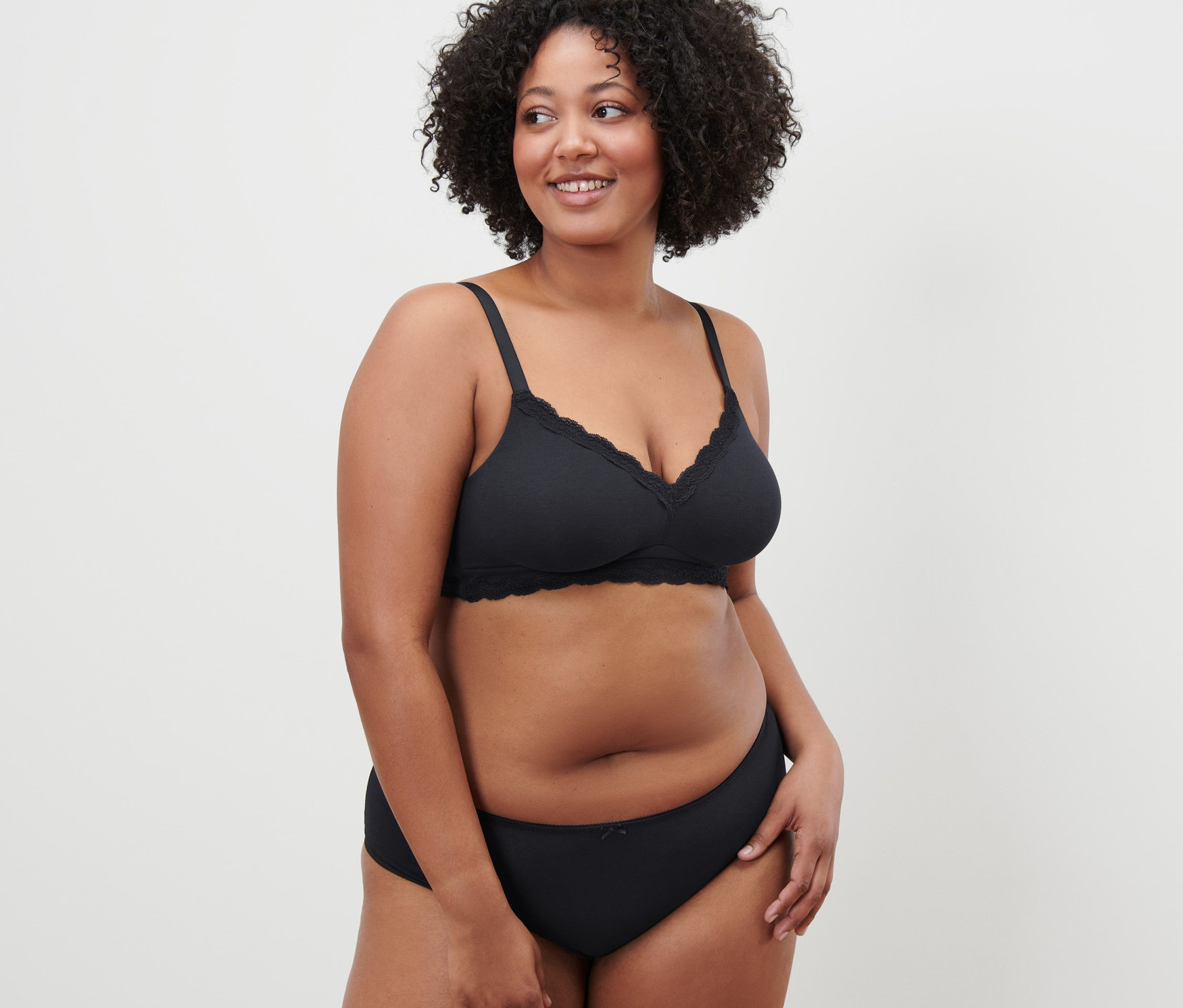 Žena s kudrnatými vlasy pózuje v černé měkké podprsence.