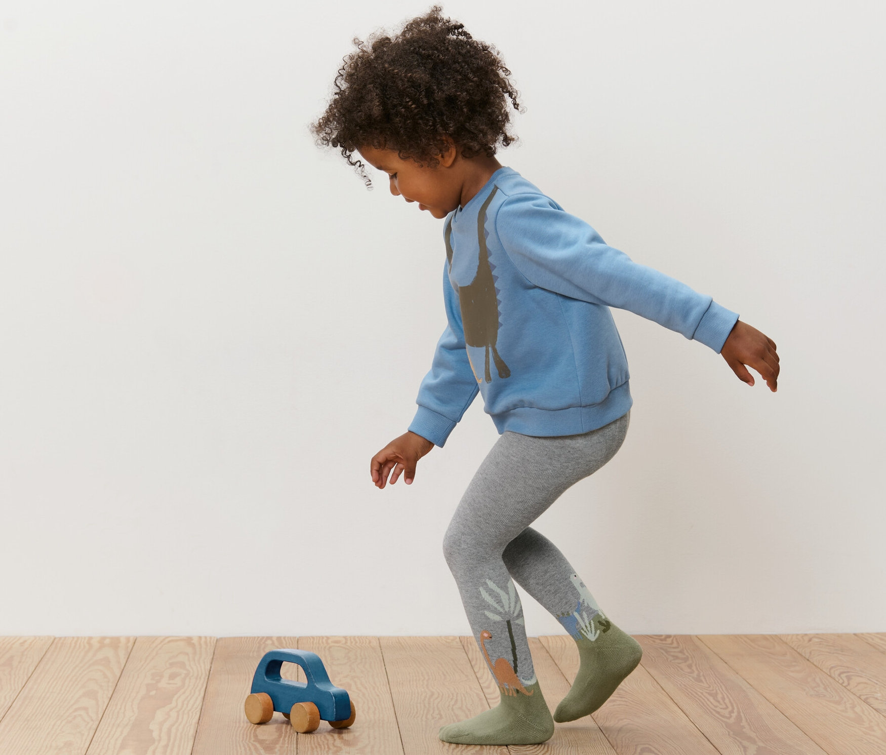 Dítě si hraje s modrým dřevěným autíčkem a má na sobě modrou mikinu a šedé punčocháče Dětské punčocháče, 3 páry, modrá.
