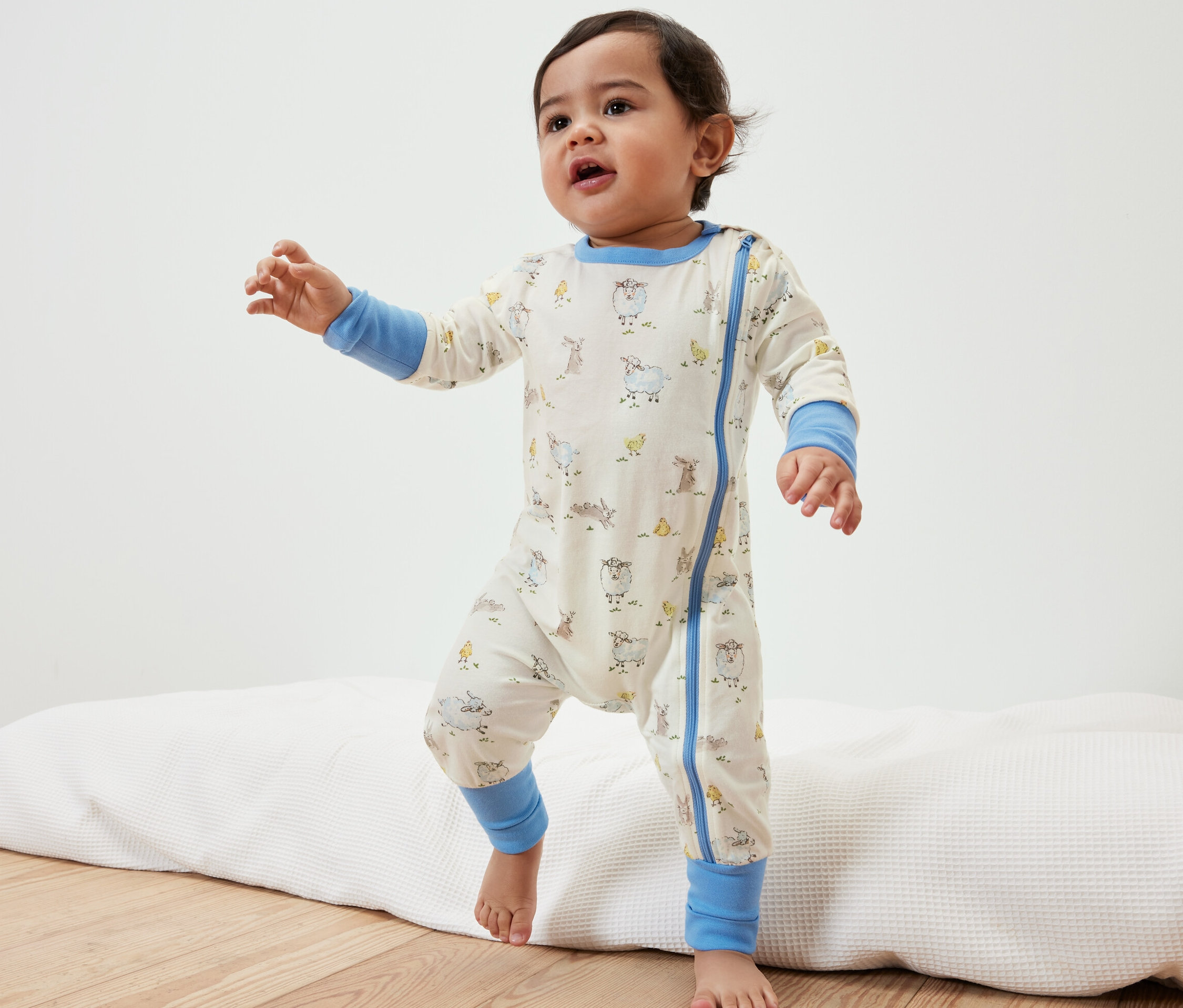 Batole v pyžamu se zvířátky stojí na podložce.