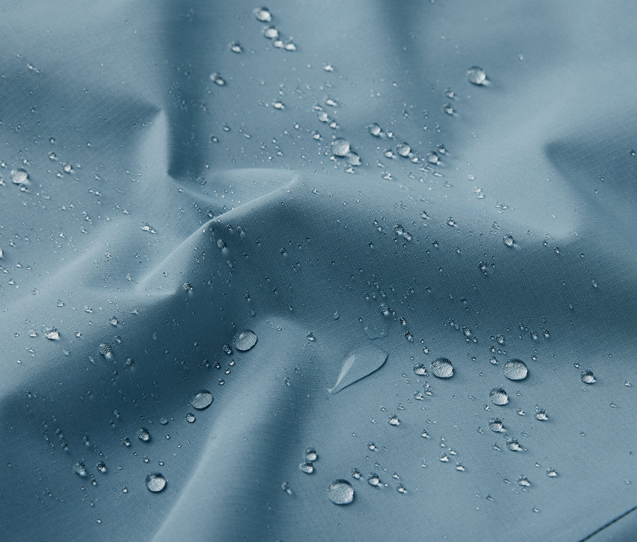 Detailní záběr na modrou funkční outdoorovou bundu s kapkami vody.