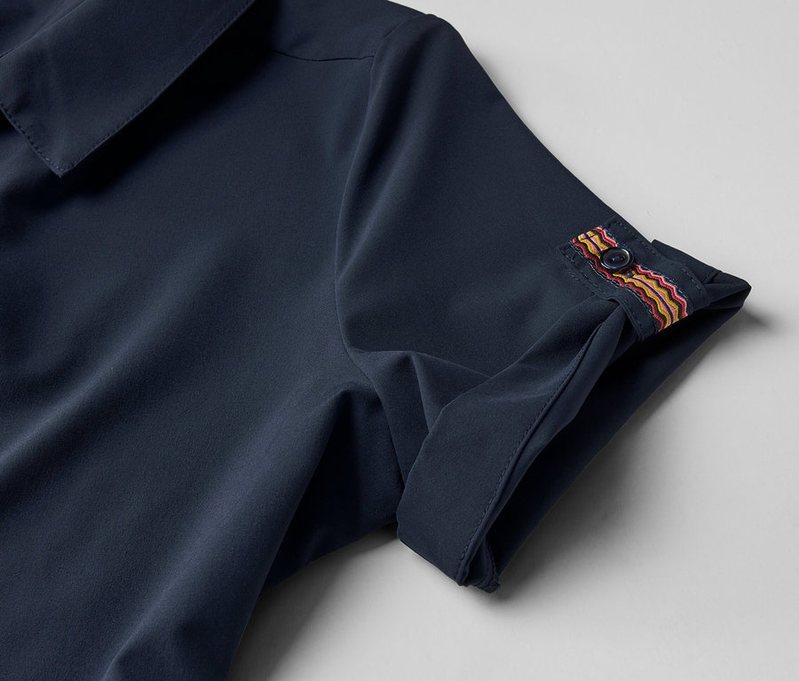 Detail funkčních šatů s knoflíkem na rukávu.