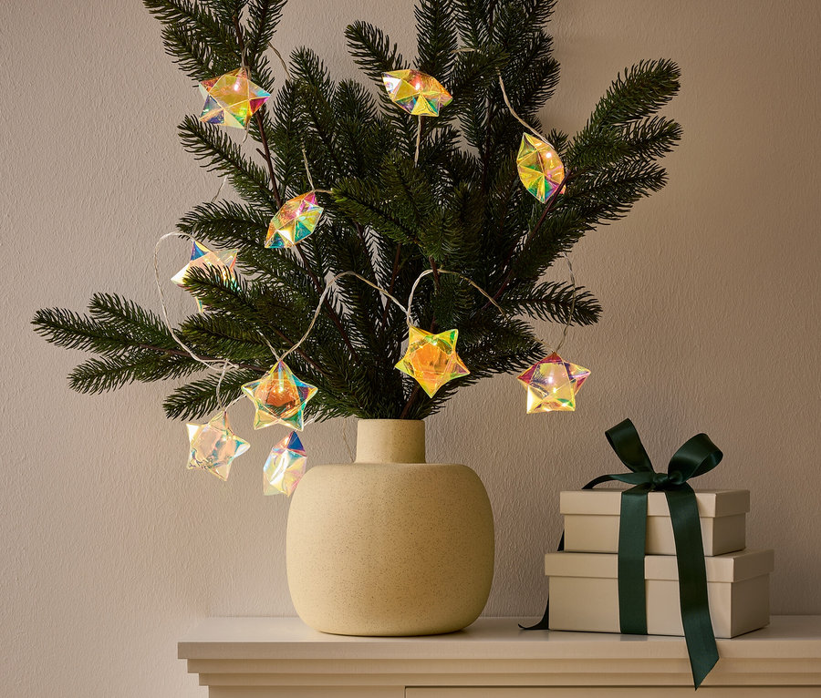 Váza s větvičkou zdobenou světelným řetězem ve tvaru hvězdy stojí na skříňce vedle dvou dárkových krabic s tmavě zelenou stuhou.