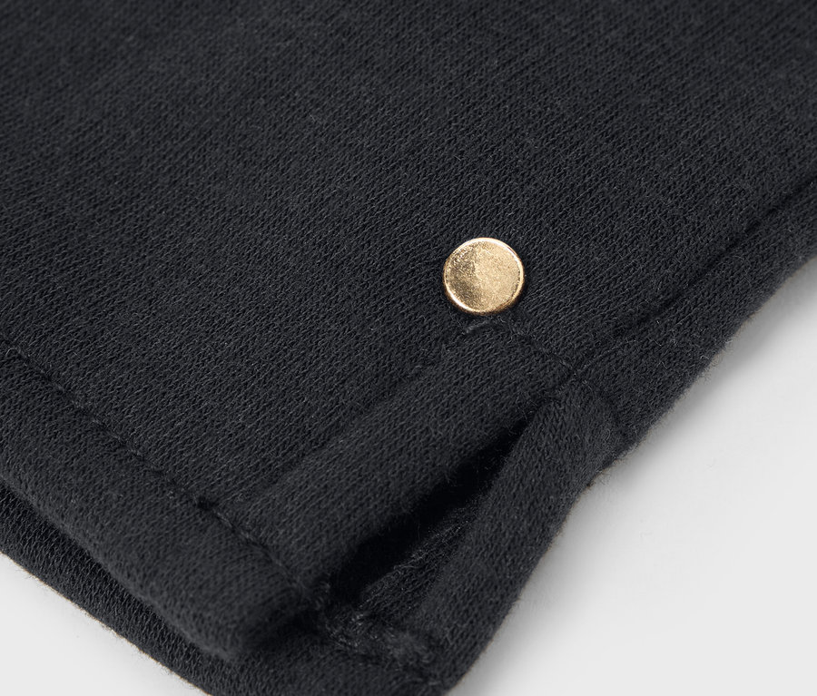 Detailní záběr na černou látku s malým zlatým knoflíkem.