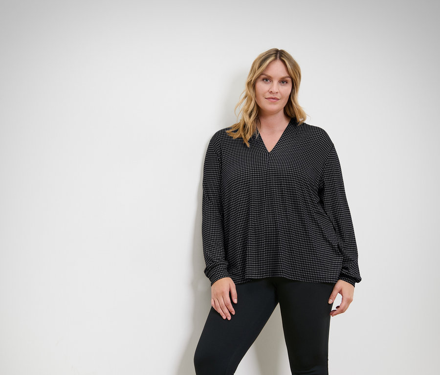 Žena pózuje ve vrchním dílu a kalhotách černé barvy.