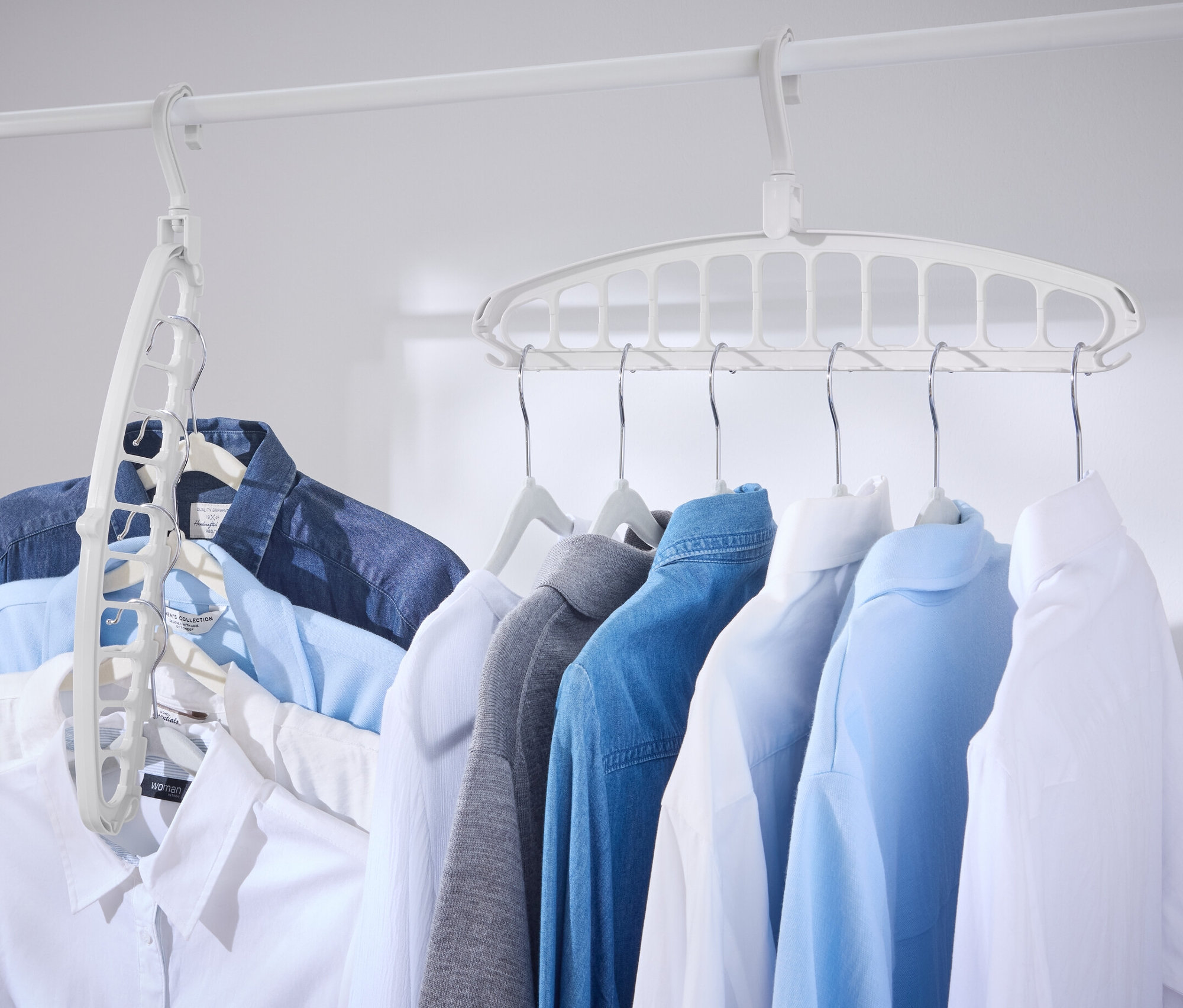 Na bílé tyči visí bílé multifunkční ramínko na šaty a několik košil.