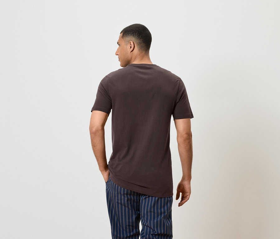 Muž zády k fotoaparátu má na sobě hnědé tričko a modré pruhované kalhoty.