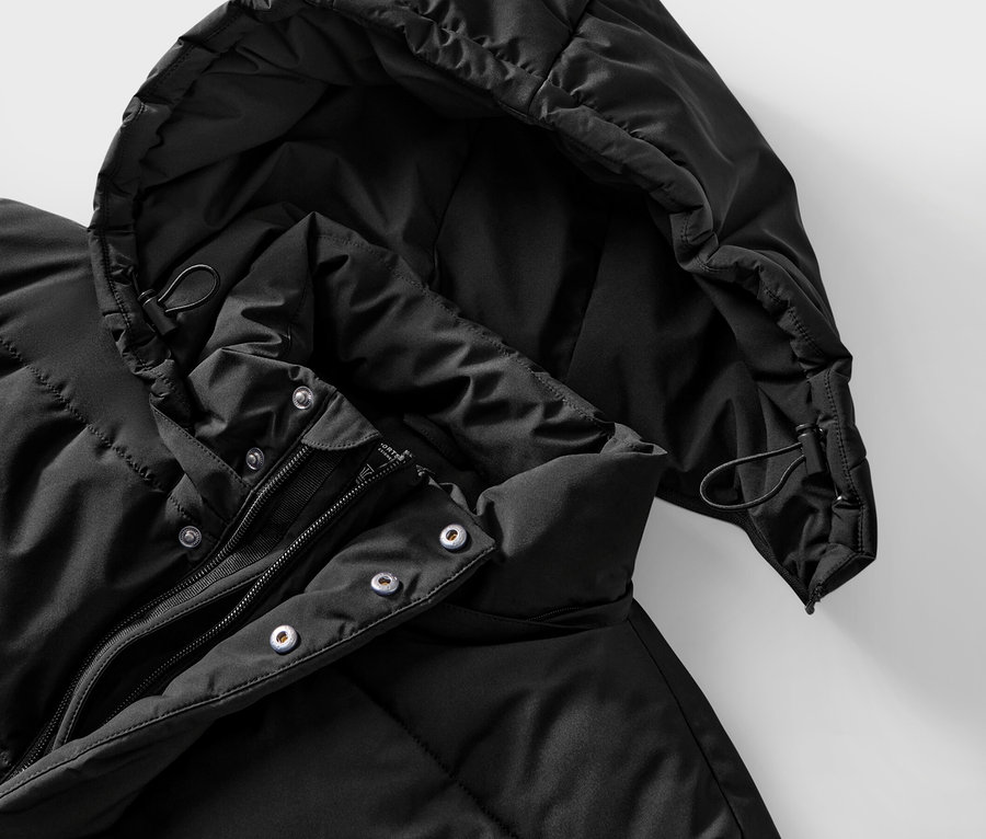 Detail černé prošívané bundy s kapucí a zipem.