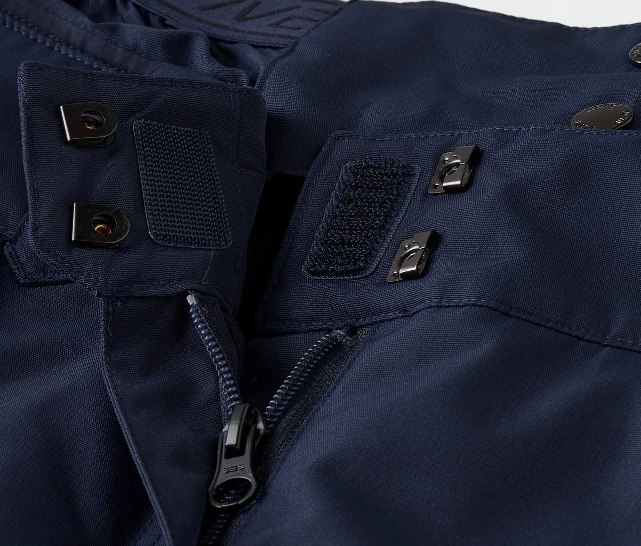 Detail modré bundy se zipem, suchým zipem a knoflíky.